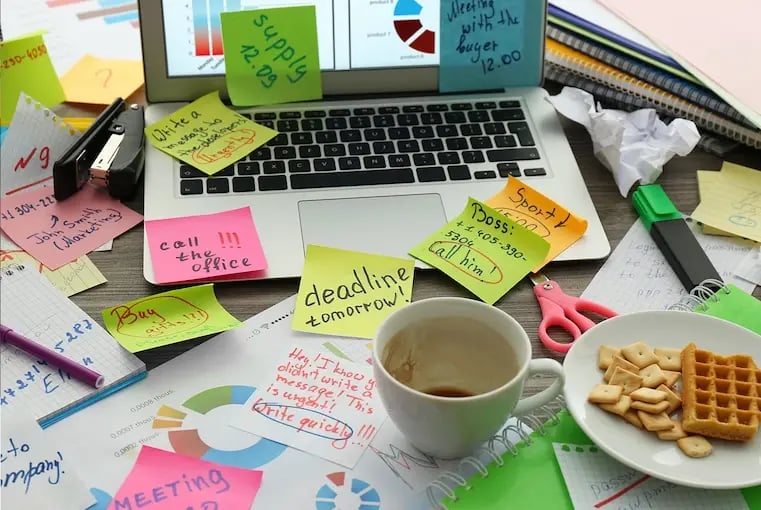 Desk with laptop full of sticky notes, waffles and empty cup of a coffee