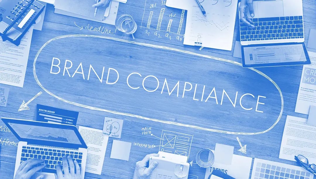 Desk with office laptops, assets and huge brand compliance sign on it