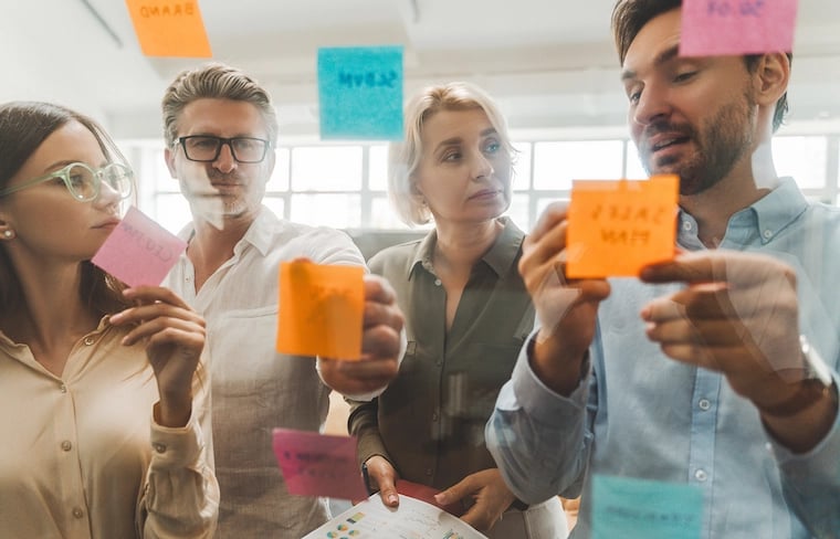 Marketing operations people planning out system with use of sticky notes at the glass