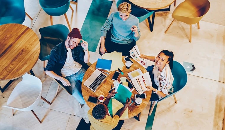 Overhead, top-down shot of creatives chatting at work by the coffee table