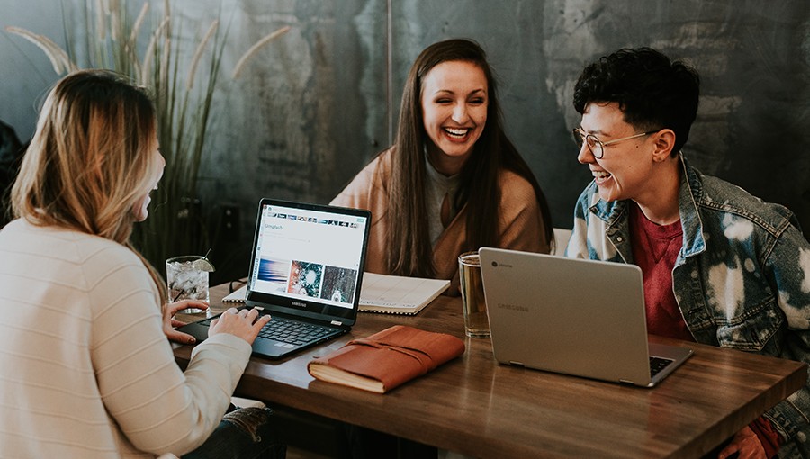 Young business adults laughing and coworking by the table with laptops